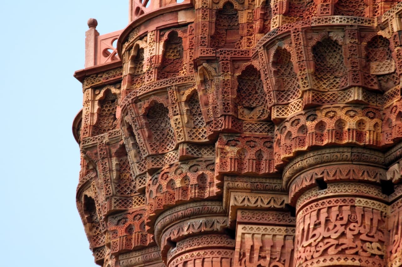 Close-up detail of Qutub Minar's Arabic calligraphy, carved geometric patterns and projecting balcony